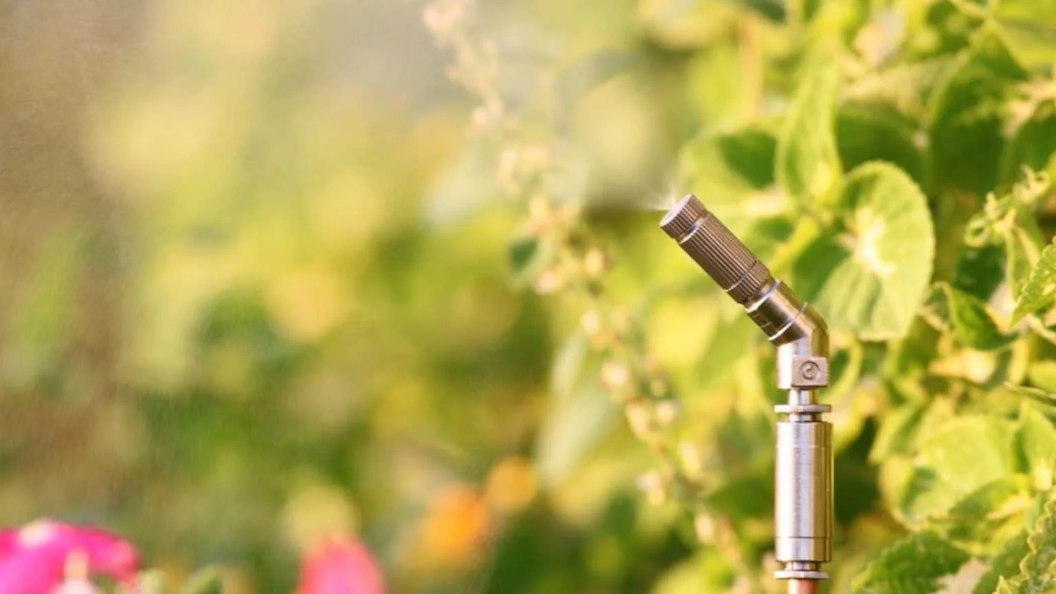 A misting nozzle sprays a fine mist in a lush green garden